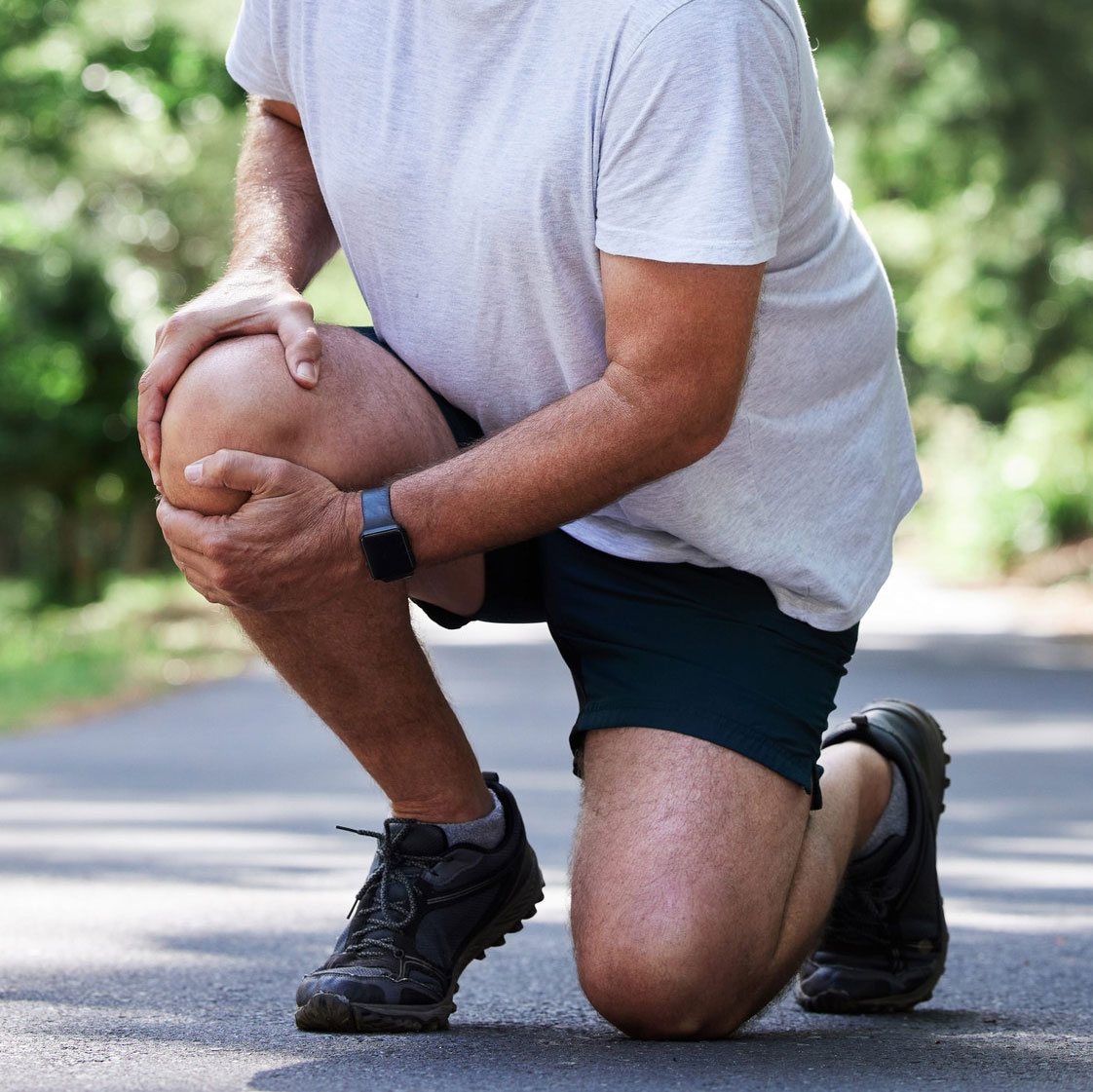 Person kneeling outdoors gripping knee in pain